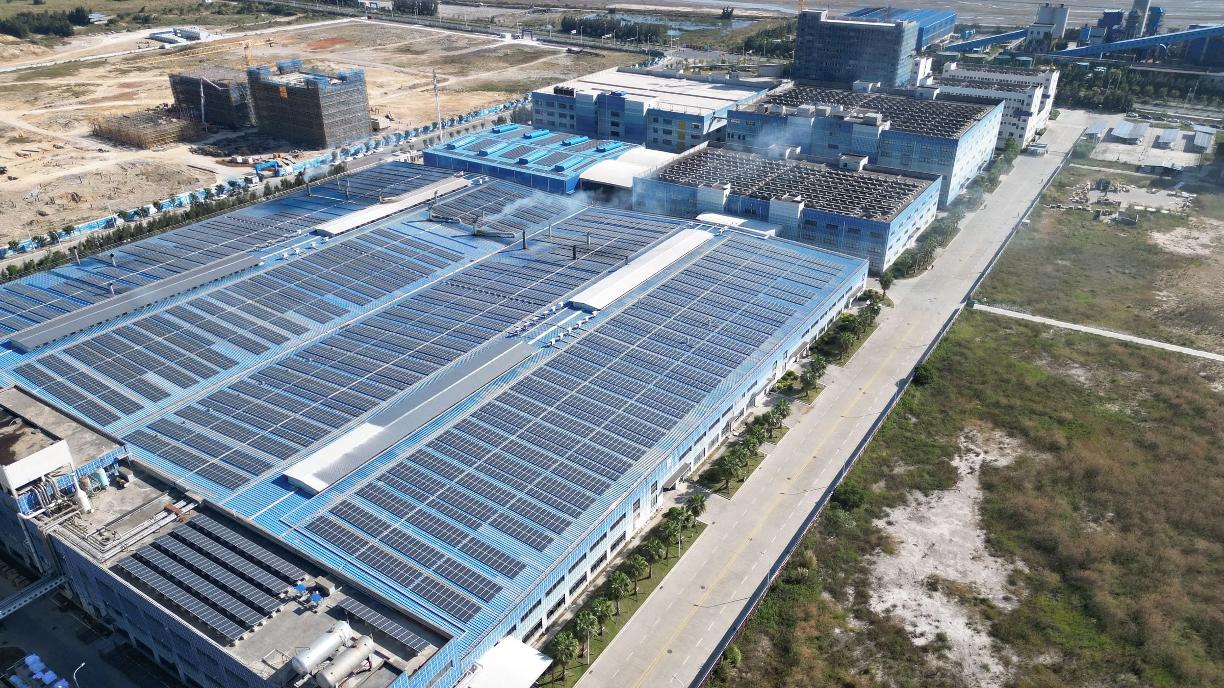 Aerial view of a large factory complex with solar arrays across its roofs